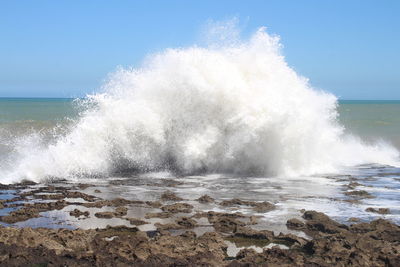 Sea waves splashing on shore against clear sky