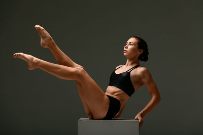 Full length of young woman exercising against colored background