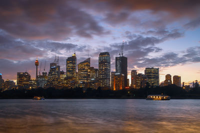 Illuminated buildings by river against sky in city