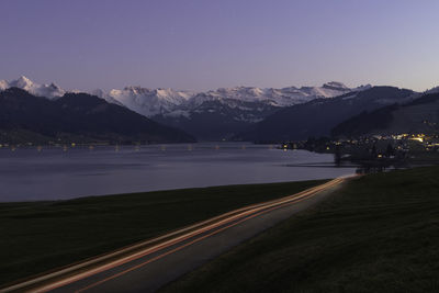 Light trails on road by mountains against sky at night