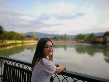 Portrait of beautiful woman standing by railing against lake