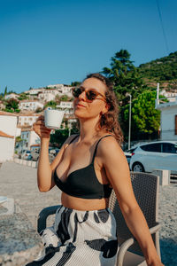 Portrait of young woman wearing sunglasses while standing against sky