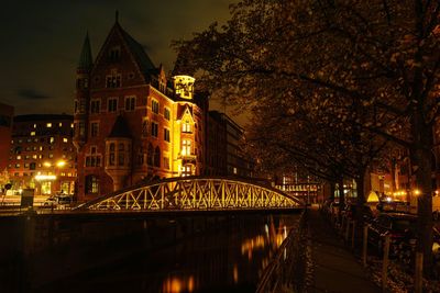 Illuminated bridge over river amidst buildings in city at night