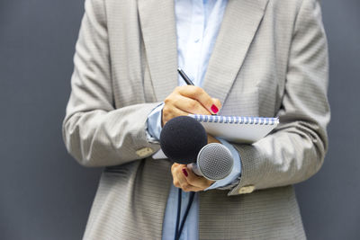 Journalist or reporter at press conference or media event, holding microphone, writing notes