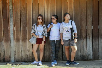 Full length of sisters standing with mother against wooden fence