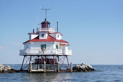 Lighthouse by sea against clear sky