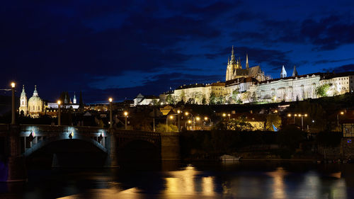 Illuminated castle by bridge over river at night