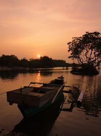 Boat moored in lake against sky during sunset