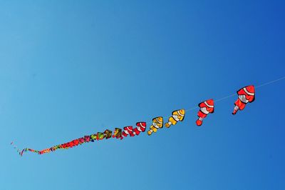 Low angle view of kites flying against clear blue sky