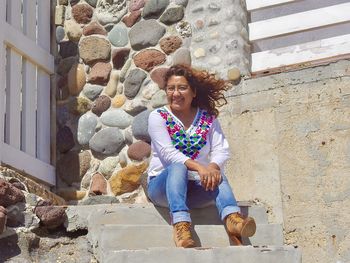 Portrait of smiling young woman sitting against wall