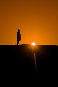 Silhouette man standing against orange sky during sunset