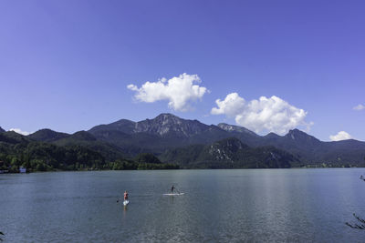 High angle view of people paddleboarding on kochelsee lake against blue sky