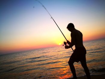 Man fishing at beach during sunset