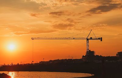 Silhouette cranes at construction site against sky during sunset