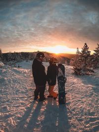 Rear view of people standing on snow during sunset