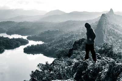 Full length of hiker standing on rock by river against sky