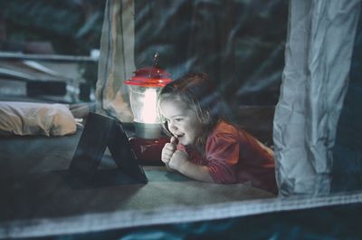 Girl looking at digital tablet by illuminated lantern on bed at home