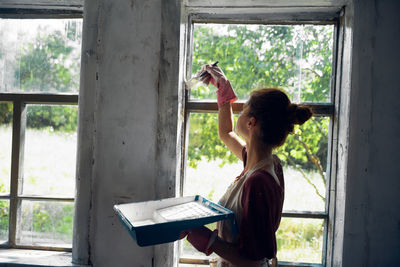 Side view of young woman painting wall