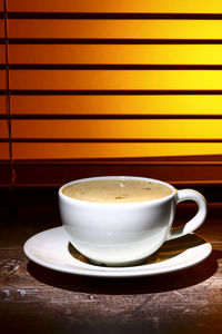 Coffee cup filled with frothy coffee set against a window blind