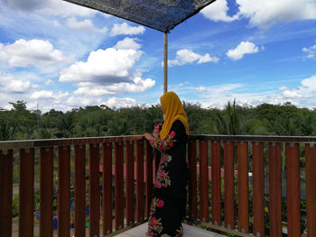 Rear view of woman standing by railing against sky