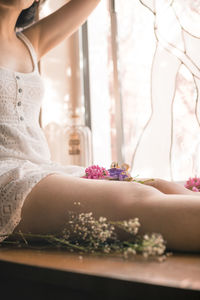 Midsection of woman sitting with flowers at home