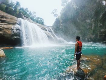 Rear view of man standing on rock against waterfall