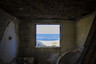 Abandoned building by sea against sky seen through window
