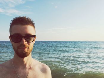 Portrait of young man wearing sunglasses while standing at beach against sky