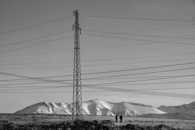 Electricity pylons on snowcapped mountain against sky