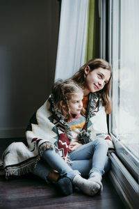 Mother and girl sitting on window at home
