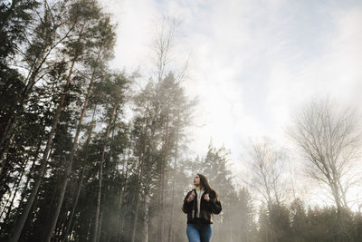 Low angle view of woman walking in forest during foggy weather