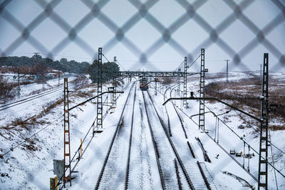 Snow covered railroad tracks by plants during winter