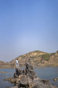 Young indian boy standing on a cliff near a landscape of a lake and mountain in the background.