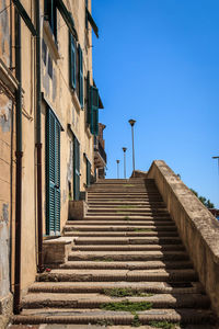 Low angle view of steps amidst buildings against clear blue sky