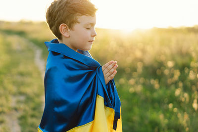 Ukrainian boy closed her eyes and praying to stop the war in ukraine in a field at sunset