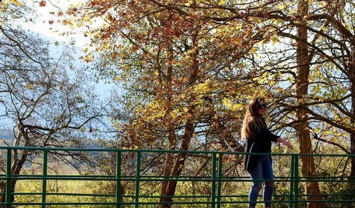 Woman standing by tree against sky during autumn