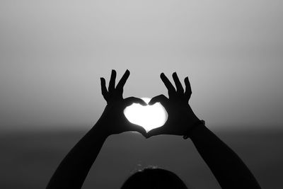 Woman making heart shape against sun at sunset