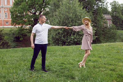 Man and a woman in love in a dress and hat are dance on a green field under a tree in summer