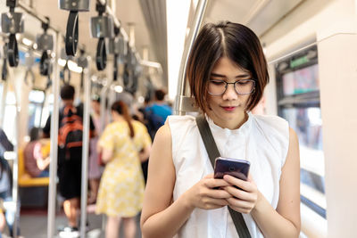 Asian young short hair woman wearing glasses using and looking her smartphone in train