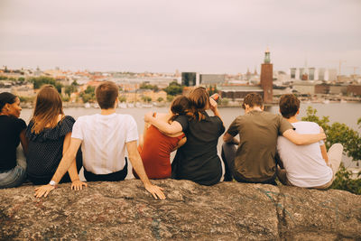 Rear view of people sitting on walkway in city against sky