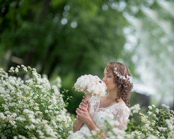 Bride smelling flower bouquet while standing by plants