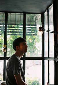 Side view of young man looking at illuminated light bulb by window