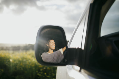 Happy young woman driving van seen through side-view mirror