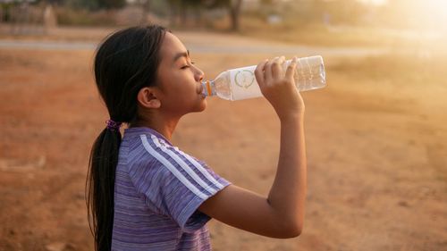 Side view of girl drinking water from bottle