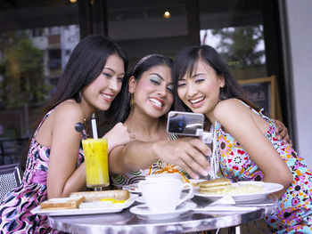 Cheerful friends taking selfie with smart phone at restaurant