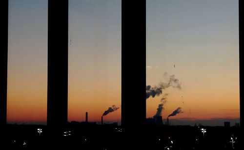 Silhouette smoke emitting from factory against clear sky during sunset