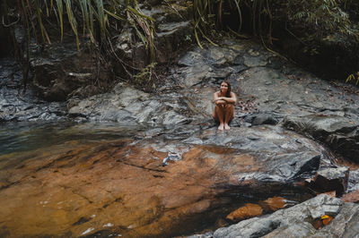 Full length of shirtless man standing on rock in river