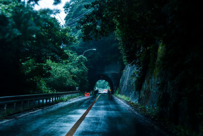 Empty wet road leading toward tunnel amidst trees during rainy season