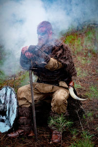 Full length of man wearing costume sitting on field in forest