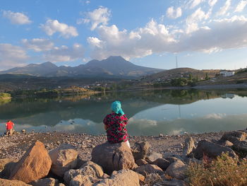 Rear view of man looking at lake against sky